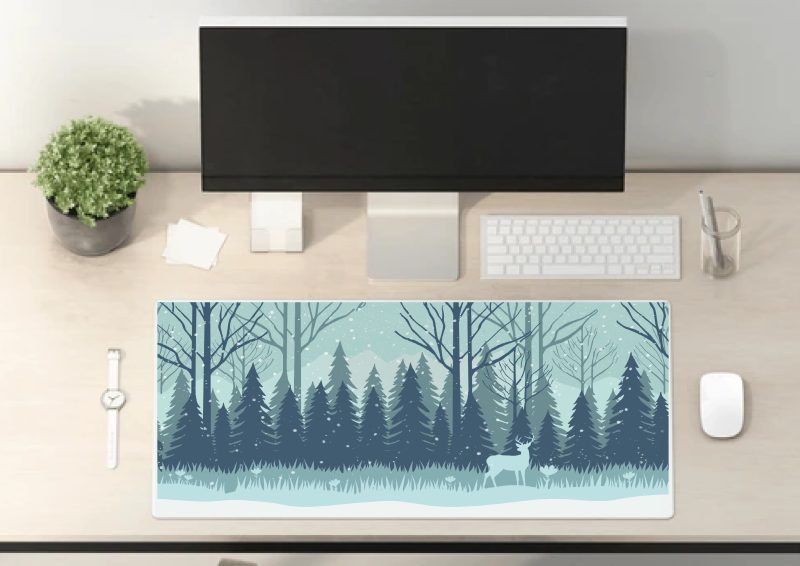 Mockup of a desk mat illustration, white and blue colours of a snow landscape, trees and mountains. Deer is in foreground.